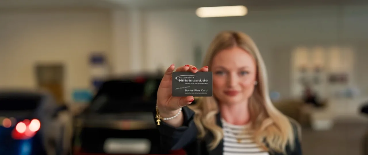 Mitarbeiterin von Automobile Hillebrand hält die Bonus Plus Card (Kundenkarte) in die Kamera